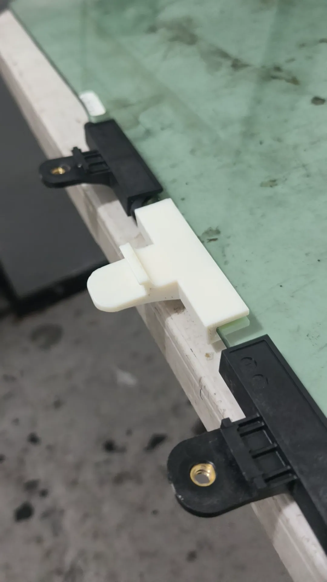 Base nueva impresa en 3D, en blanco, junto a una base original negra sobre el vidrio del Kia K4
